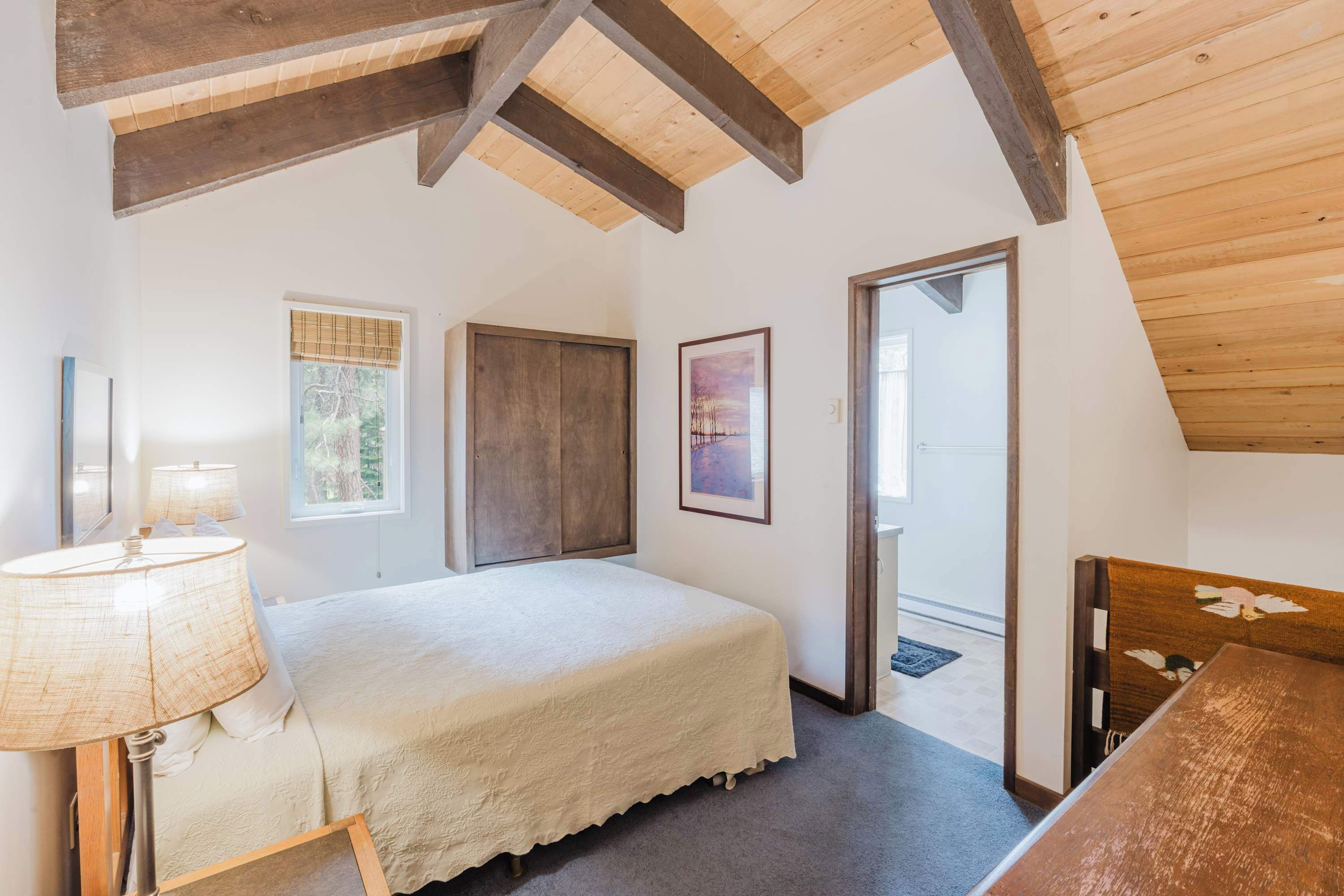 Een slaapkamer met een bed, een houten hoofdbord, een nachtkastje, een lamp, een raam en een deur.