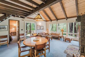 Una habitación amplia con una mesa de madera para comer, sillas, un sofá y un gran ventanal con vistas a árboles.
