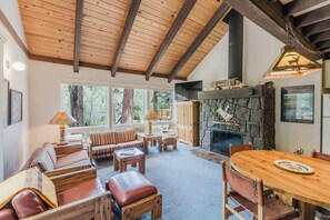 Una sala de estar acogedora con chimenea de piedra, vigas de madera en el techo y un ventanal con vistas a un bosque.