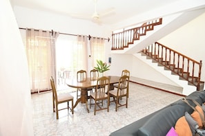 A dining area with a table and chairs, a staircase, and a living room with a sofa. - Tropical villa with a large pool, lush gardens, spacious rooms, and privacy. (Pointe Aux Cannioner)