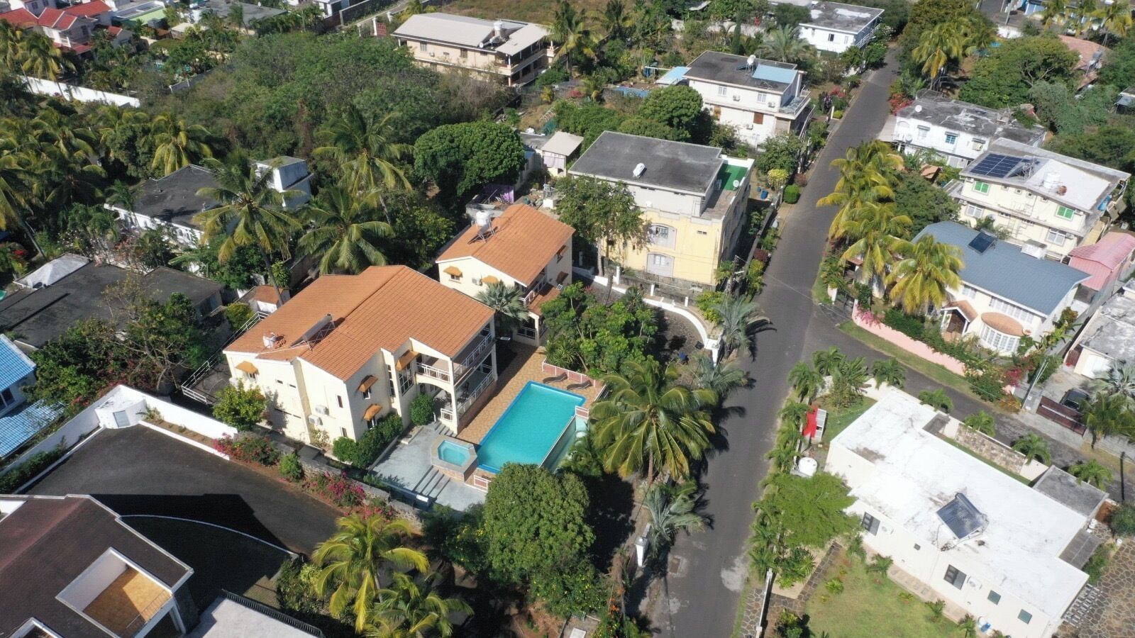 Oversigtsbillede af et boligområde med huse, en swimmingpool og palmer.