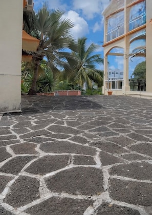 A paved courtyard with palm trees, a building with balconies, and a clear sky. - Tropical villa with a large pool, lush gardens, spacious rooms, and privacy. (Pointe Aux Cannioner)
