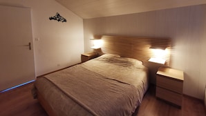 Ein Schlafzimmer mit einem hölzernen Kopfende, zwei Nachttischen, einem Bett mit gemustertem Überwurf und einer wandmontierten Leuchte.
