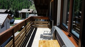 Ein Balkon mit Holztisch und zwei Stühlen, mit Blick auf eine Berglandschaft mit Häusern.