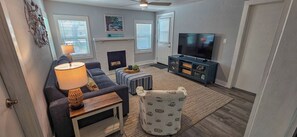 Ein Wohnzimmer mit Sofa, Hocker, TV-Stand, Kamin und Deckenventilator.