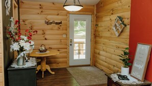 A wooden interior with a door, a table with a vase of flowers, a small cabinet, and a framed sign on the wall. - Lovely 4-bedroom cabin with AC in pleasant Shoals (Shoals)
