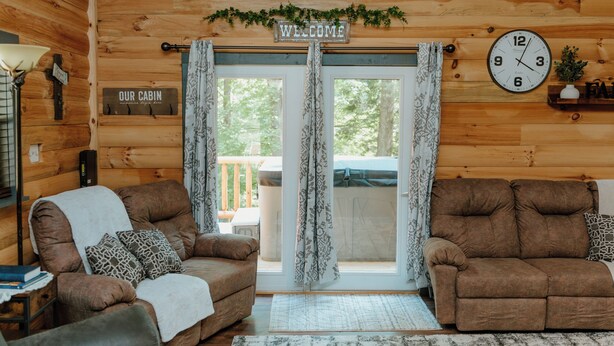 A cabin interior with two sofas, a welcome sign, a clock, and a 'Our Cabin' sign. - Lovely 4-bedroom cabin with AC in pleasant Shoals (Shoals)