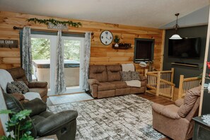 Ein Ferienhäuschen im Inneren mit einer Couch, Sesseln, einem Fernseher, Holzwänden, einer Uhr und einem Willkommensschild.