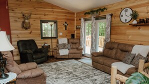 A log cabin interior with a fireplace, leather furniture, a clock, and a view to the outside. - Lovely 4-bedroom cabin with AC in pleasant Shoals (Shoals)