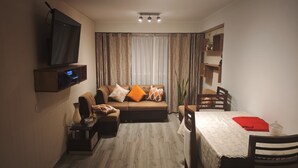 Ein Wohnzimmer mit Sofa, Fernseher, Esstisch und Stühlen.