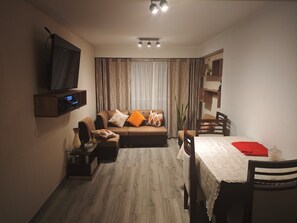 A living room with a sofa, TV, dining table, and chairs. - 1-BEDROOM APARTMENT (Lima)