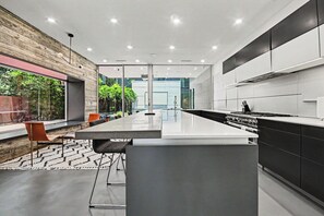 A modern kitchen with a central island, black cabinetry, and a view of greenery outside. - Luxury Houston Home! (Houston)