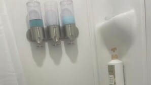 A bathroom with three clear glass dispensers, a white bottle on a shelf, and two smaller bottles on a lower shelf. - Tiny House near Hillsdale College (Hillsdale)