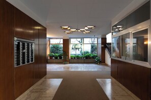 A modern hotel lobby with wooden paneling, a central staircase, and a view of greenery through large windows. - Maggi Milano - Design retreat in Milan’s most desirable neighborhood. (Milano)