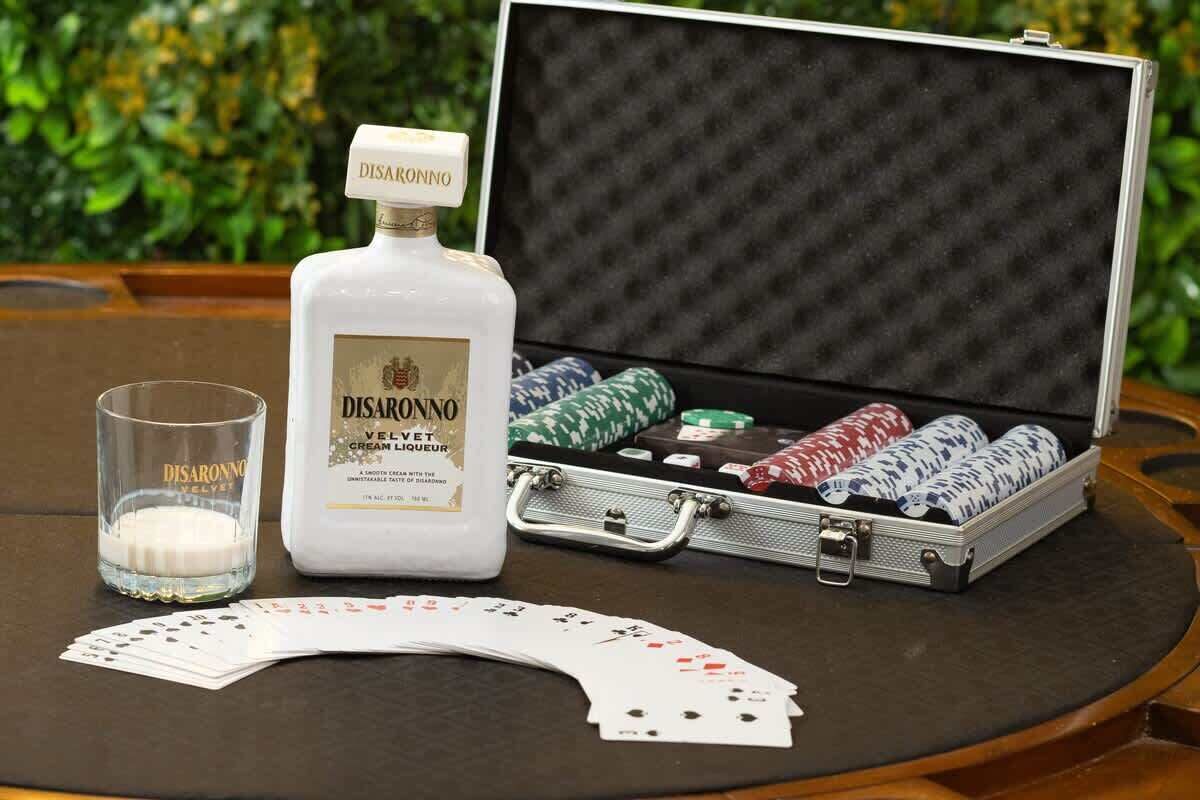 Une bouteille de liqueur Disaronno VELVET Cream, un verre de la même liqueur, et un jeu de poker avec des cartes, le tout posé sur une table.