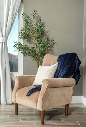 Un fauteuil beige aux pieds en bois, un coussin blanc et un plaid bleu.