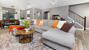 A modern living room with a grey sectional sofa, a round coffee table, and a chandelier. - Heated Pool • Game Rm • Theater • Firepit • Pets (San Antonio)