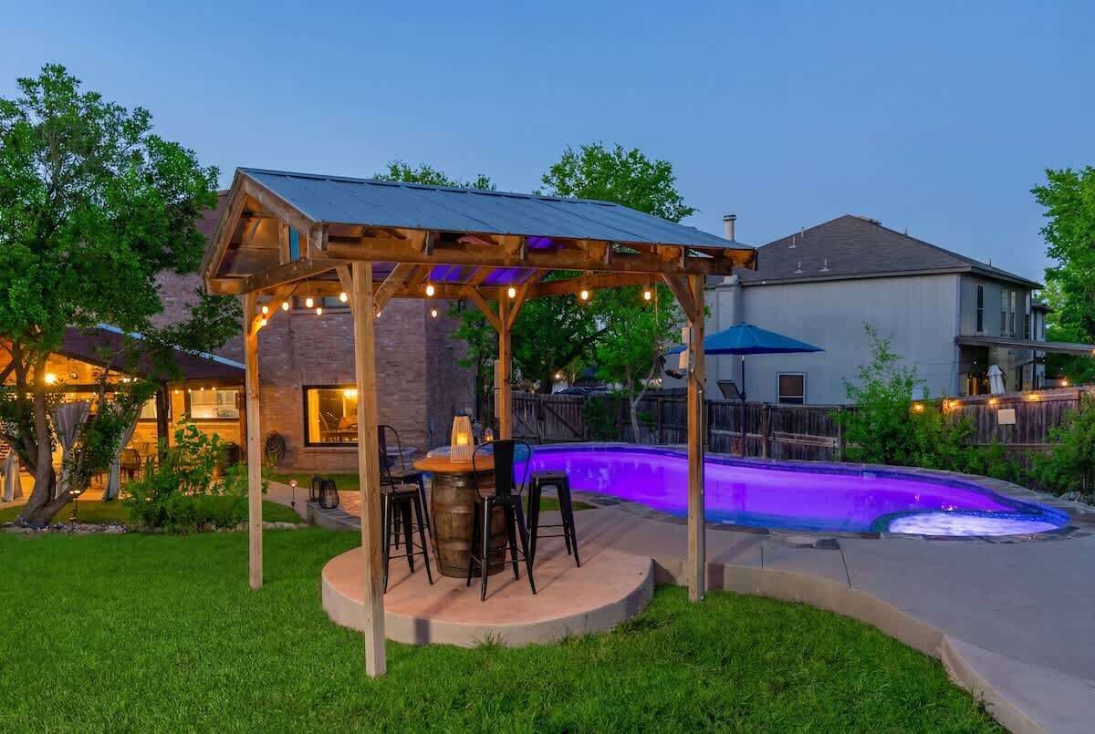 Ein Garten mit einer hölzernen Pergola, einem Whirlpool und einem Essbereich mit Stühlen und Tisch.