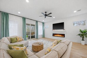 Ein Wohnzimmer mit einer Sofagarnitur, einem runden Couchtisch, einem Flachbildfernseher, einem Kamin und einem Deckenventilator.