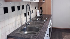 Een moderne keuken met een roestvrijstalen spoelbak, houten keukenkastjes, een betegelde spatwand en een inbouwoven.