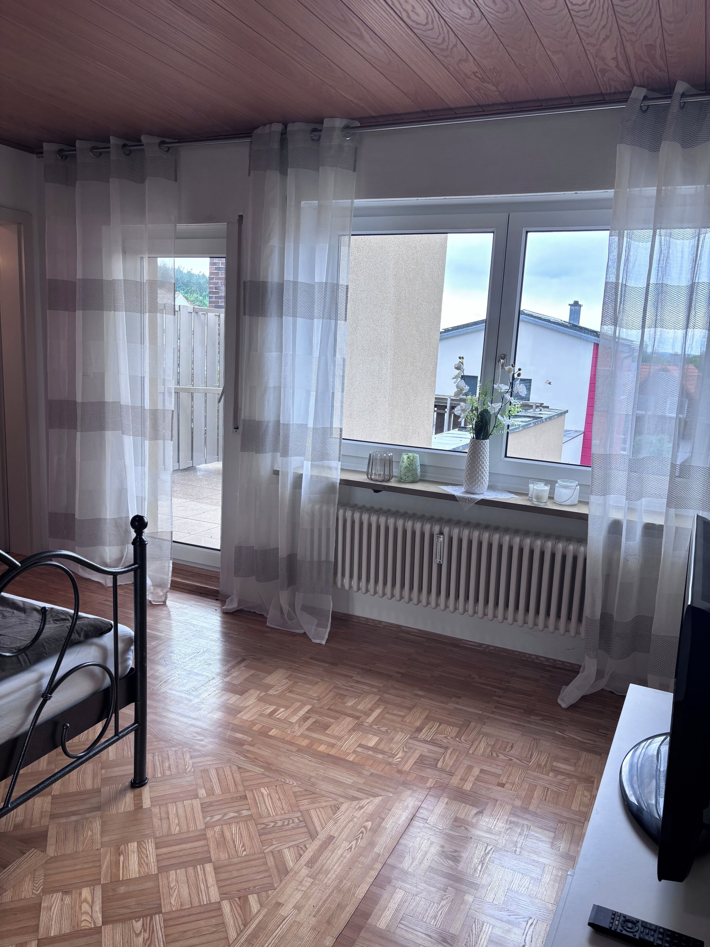 A room with a bed, a radiator, a window with curtains, and a television.