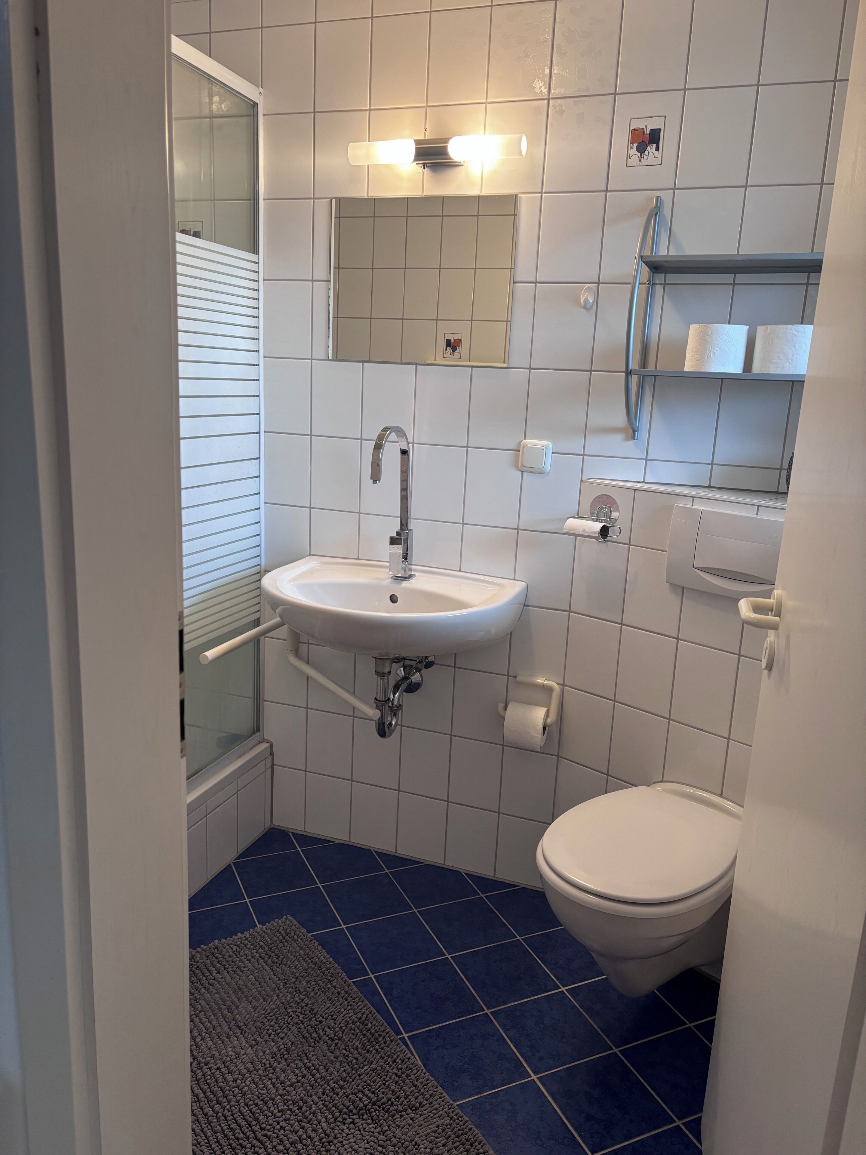 Une salle de bain avec un lavabo blanc, des toilettes, une douche et un miroir.