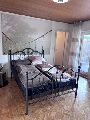 A room with a bed, a wall mural, a door, and a window.