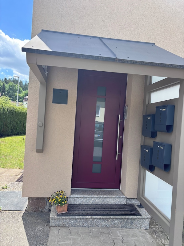 A building entrance with a red door, a mailbox, and a small flower pot.