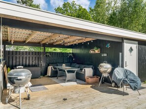 Eine Terrasse im Freien mit überdachter Sitzgruppe, Grill und Holzdeck.