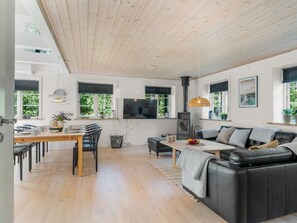 Ein modernes Wohnzimmer mit Holzboden, einem schwarzen Ledersofa, einem Esstisch mit Stühlen und einem an der Wand befestigten Fernseher.