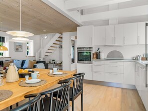 Een moderne keuken met witte kastjes, een inbouwoven en een eethoek met een houten tafel en stoelen.