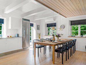 Een moderne keuken met witte kasten, een roestvrijstalen koelkast, en een eethoek met een houten tafel en zwarte stoelen.