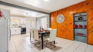 Une cuisine moderne avec des meubles blancs, une table à manger avec des chaises et un mur d’accent en bois.