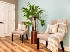 Una habitación con dos sillones, una planta grande en maceta y una puerta.