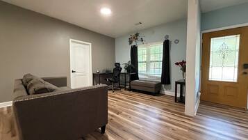 A living room with a sofa, a desk with a chair, a window with curtains, and a door with a stained glass window.