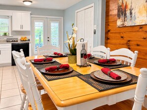 A dining area with a wooden table set for four, white chairs, and a kitchen in the background.