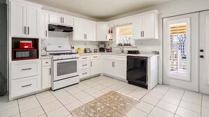A kitchen with white cabinets, a stove, microwave, and dishwasher. - Comfortable 4BR•2 King Beds• Near Arbor Place Mall (Douglasville)