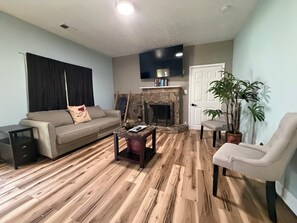 A living room with a sofa, armchair, coffee table, fireplace, and a potted plant.