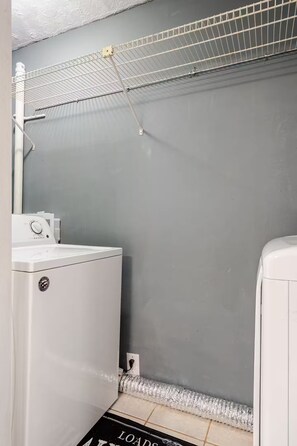 Un espace buanderie comprenant un lave-linge, un étendoir et un sol carrelé.