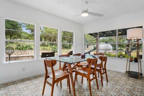 Comedor con mesa de vidrio y sillas de madera, ventanas amplias con vistas a zonas verdes y un ventilador de techo.
