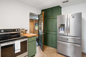 A kitchen with a stove, oven, green cabinets, and a stainless steel refrigerator.