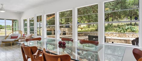 A spacious room with a glass table and chairs, large windows, and a view of the outdoors.