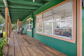 Un porche cubierto con piso de madera, paredes verdes y ventanas amplias.