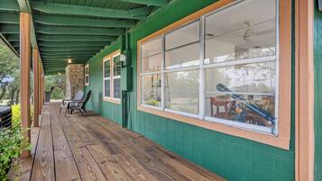 A covered porch with wooden flooring, green walls, and large windows.