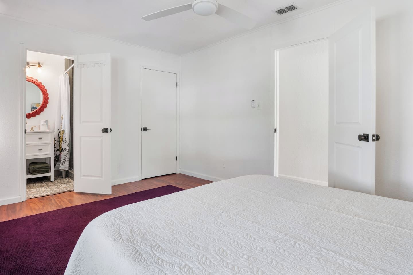 A bedroom with a bed, a door, a mirror, and a ceiling fan.