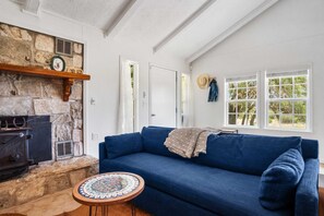 Una sala de estar acogedora con chimenea de piedra, un sofá azul y una mesa redonda con tablero estampado.