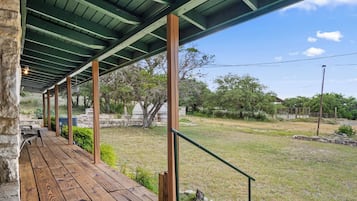 A covered outdoor area with a wooden deck, stone walls, and a view of a grassy landscape with trees.