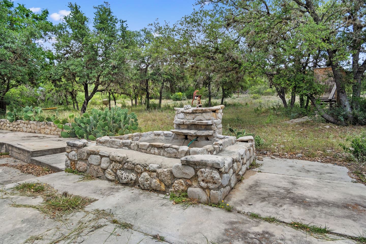 A stone structure with steps leading up to it, surrounded by greenery and trees.