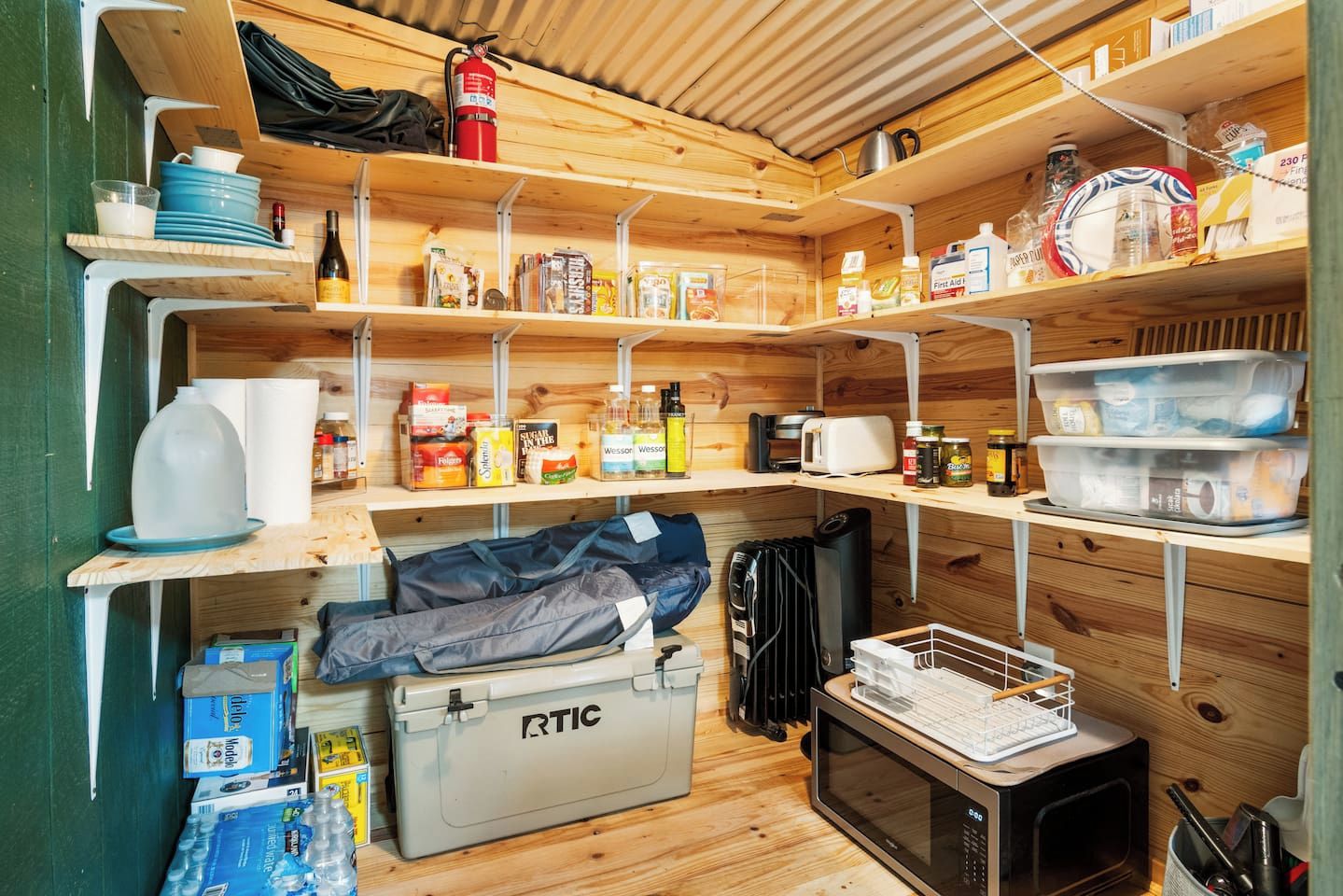 Una cocina compacta con estantes llenos de provisiones, un microondas y una estufa de gas portátil.
