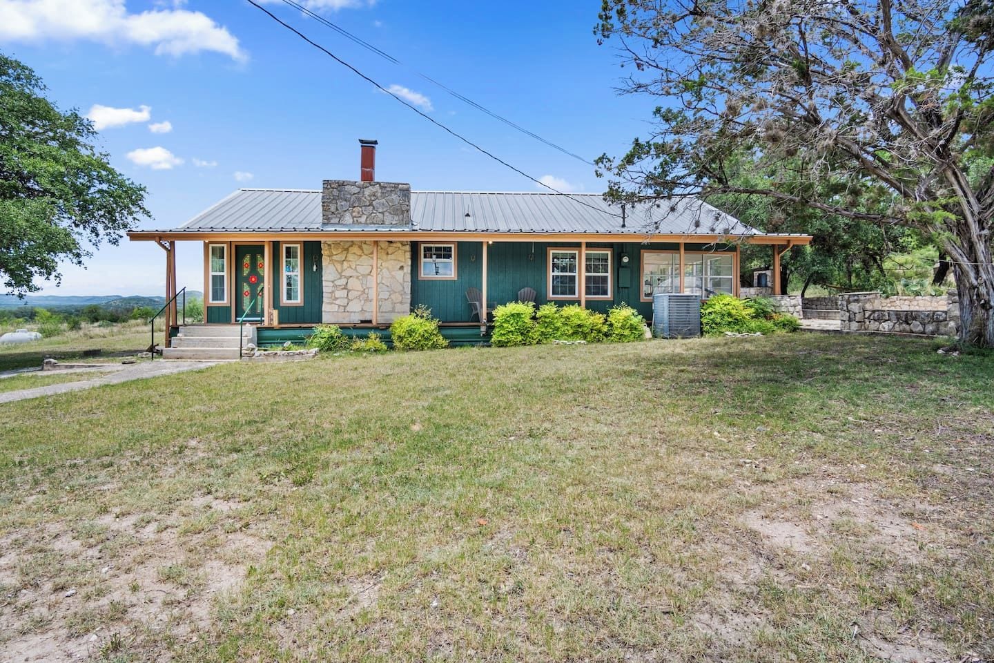 A single-story house with a stone chimney, green siding, and a front porch.